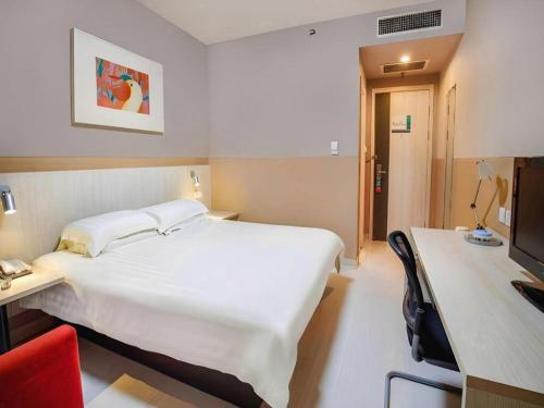 a hotel room with a large white bed and a desk at Jinjiang Inn Baotou Donghe East Railway Station in Baotou