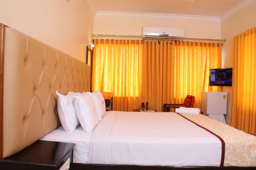 a bedroom with a large white bed with yellow curtains at Hotel Sangam in Kanyakumari
