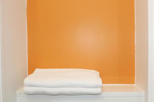 a stack of towels on a shelf with an orange wall at Première Classe Plaisir Gatines in Plaisir