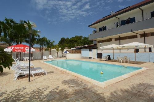 una piscina con sombrilla y sillas y un edificio en B&B La Castellana, en Marina di Ragusa