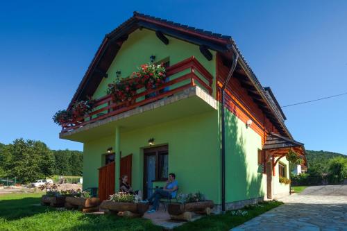 kobieta siedząca przed zielonym domem w obiekcie Plitvice Rooms w mieście Smoljanac