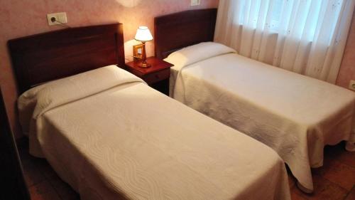 two beds in a hotel room with a lamp on a table at Apartamentos Los Balcones in Tineo