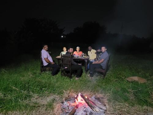 a group of people sitting around a table around a fire at Mountain View Stay in Kushālnagar