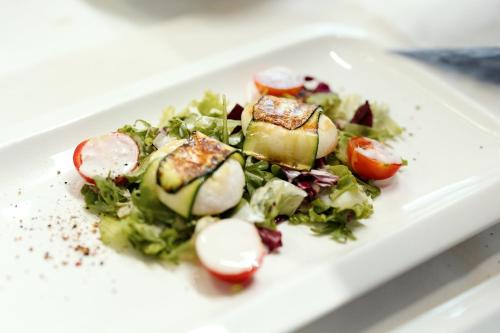a white plate with a salad with tomatoes and cucumbers at Hotel Cristallo in Santa Cristina in Val Gardena