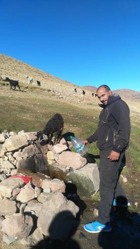 a man standing on some rocks with a bottle at Gite Oukaimeden in Oukkainrdem