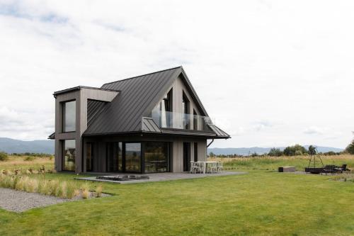 a house with a black roof on a grass field at Baniska Houses jacuzzi oraz sauna w cenie in Szaflary