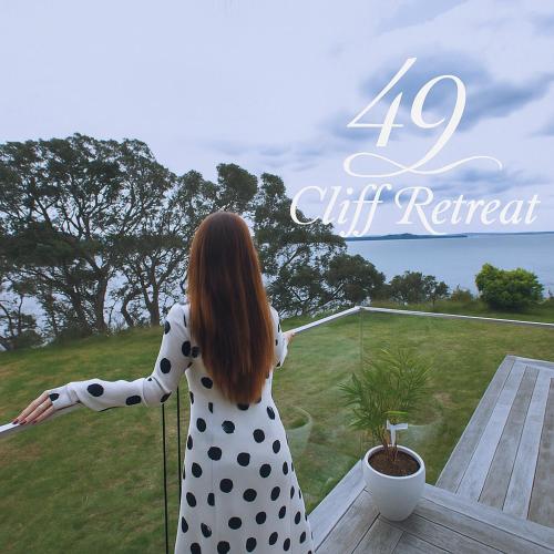 a woman in a polka dot dress standing on a balcony at 49 Cliff Retreat in Whangaparaoa