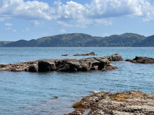 a group of rocks in the water with mountains in the background at 一日一組の宿ひめ in Kushimoto