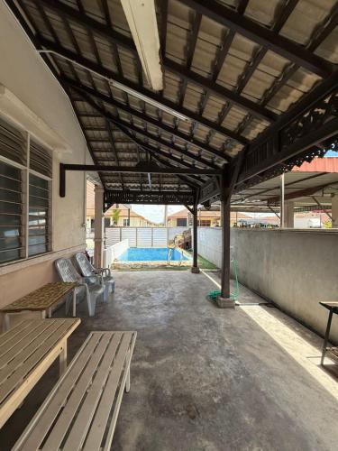 a covered patio with benches and a pool in the background at Homestay D'Putra Bertam - Homestay Kolam Bajet in Kepala Batas