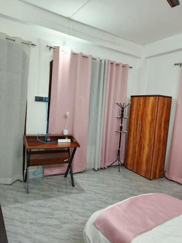 a bedroom with a desk and pink curtains and a table at Rudra Homes in Lokpriya Gopinath Bordoloi International