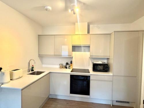 a kitchen with white cabinets and a sink and a microwave at Brand-new flat, King Bed, Sofa Bed with full kitchen, Wi-Fi, self check-in Central location near everything in Farnborough