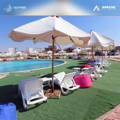 a group of chairs and umbrellas next to a pool at Santorini North Coast Resort is not for Egyptian singles in El Alamein