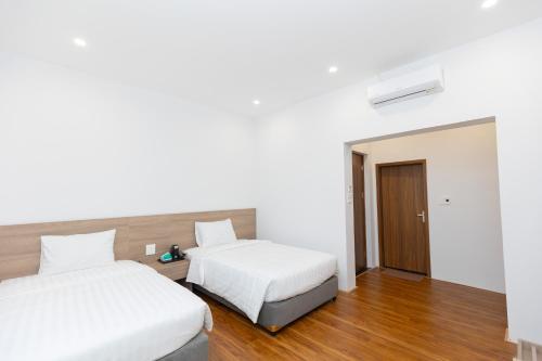 two beds in a room with white walls and wood floors at Villa Sea in Trà Cổ