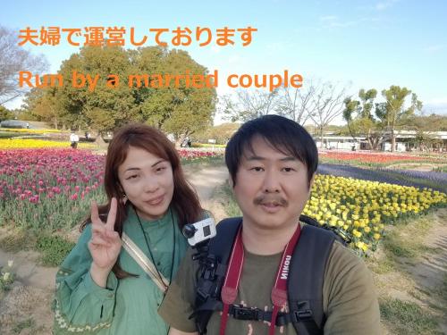 a man and a woman standing in front of a field of flowers at NINN Guest House ニン ITM Airport 大阪空港 伊丹空港 in Ikeda