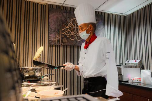 a chef wearing a mask holding a pan in a kitchen at Grand Plaza Badr Al Maqam Fully Renovated in Al Madinah
