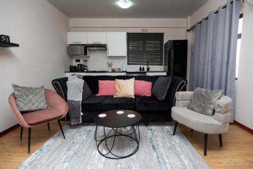 a living room with a black couch and two chairs at D12 Premier Stay in Gaborone