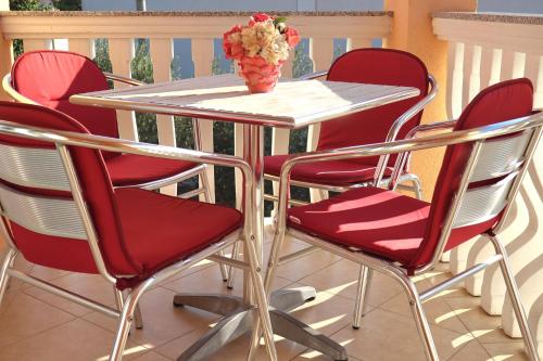 a table with red chairs and a vase of flowers at Apartmani California in Starigrad-Paklenica