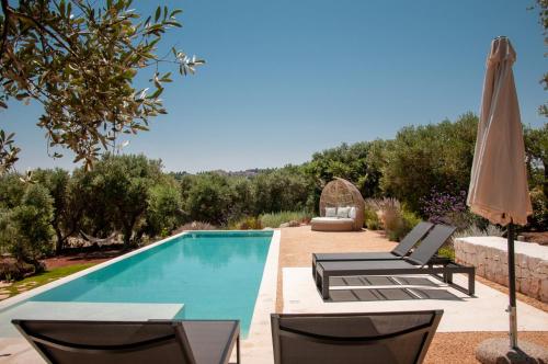 a swimming pool with two lounge chairs and an umbrella at Trulli Moranera in Cisternino