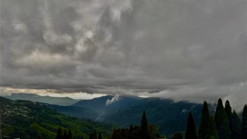 a view of a mountain range with clouds and trees at Pines and Beyond cottage in Simāna Basti