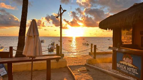 a sunset on the beach with a table and an umbrella at Morro Beach Hotel in Morro de São Paulo