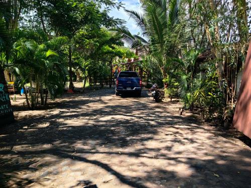a blue truck parked on a dirt road with palm trees at Cabañas kai in Iztapa
