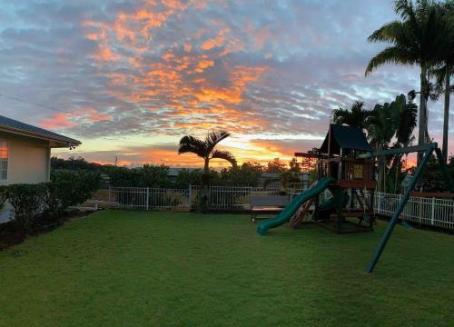 a playground with a slide in a yard with a sunset at Tropical Retreat GuestHouse in Hilo