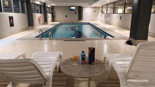 a pool with chairs and a table with a drink on it at GRU Airport Hotel - STAY HERE in Guarulhos