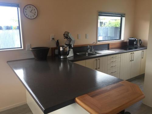 a kitchen with a black counter and a clock on the wall at Warm Cosy holiday home right in town in Raglan