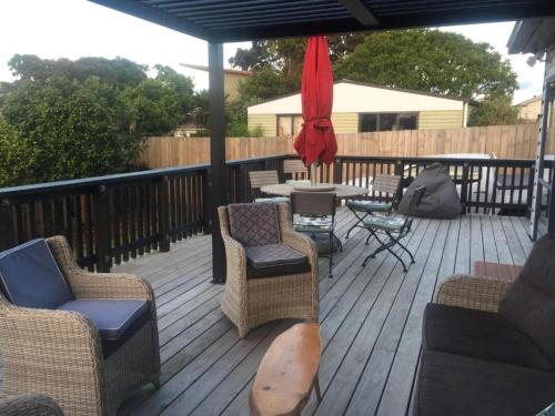 a deck with chairs and a table and an umbrella at Warm Cosy holiday home right in town in Raglan