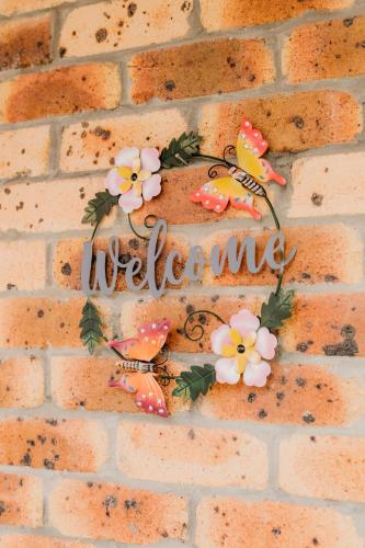 a welcome sign on a brick wall with flowers at Kennedy Drive Boutique Motel - Close To City Centre & Airport in Tweed Heads
