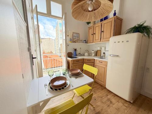 een keuken met een witte koelkast en een tafel en stoelen bij La Plage Studio lumineux, balcon vue mer in Les Sables-dʼOlonne