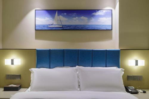 a bedroom with a bed with a picture of a sailboat on the wall at Jingtu hotel zhanjiang dingsheng plaza store in Zhanjiang