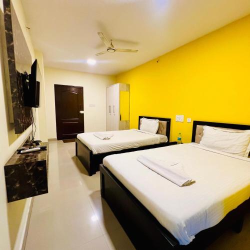 two beds in a room with a yellow wall at Janav Comforts & Suites in Bengaluru