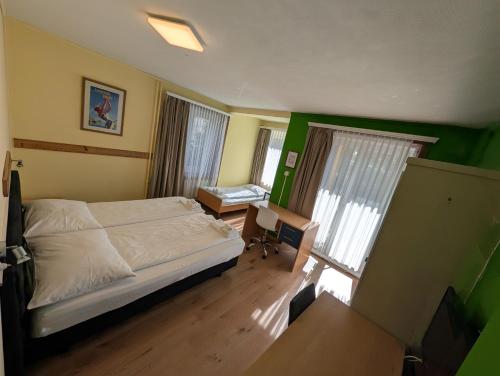 a bedroom with a bed and a desk and windows at Grischalodge das Hotel mit Bergblick seit 1929 - schlicht, preiswert und mit einem touch Nostalgie in Parpan