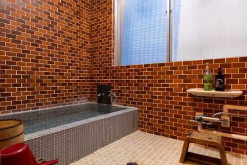 a brick bathroom with a tub and a window at Kaido Yuzawa Onsen Hostel in Yuzawa