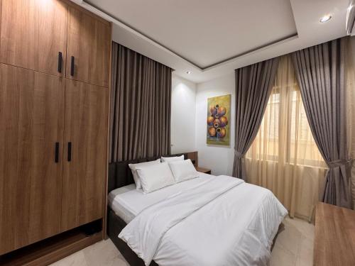 a bedroom with a white bed and a wooden cabinet at D-GioGiNiapartments in Gwarinpa