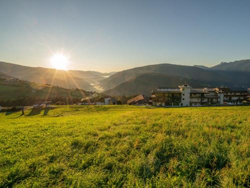a field of green grass with the sun in the background at Hotel Purvita by Oberlechner in Maranza