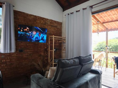 a living room with a couch and a tv on a brick wall at Vale Infinito Chalé in Córrego do Bom Jesus
