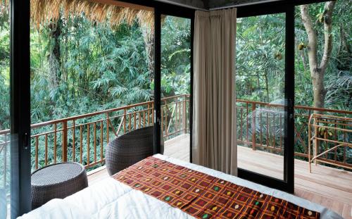 a bedroom with a bed and a balcony with windows at Ningmas Escape by Sidhi Hospitality Experiences in Ubud