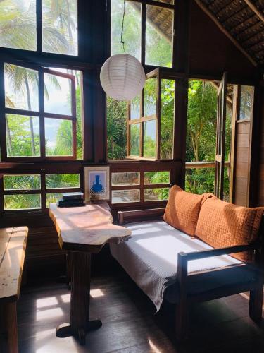 a bedroom with a bed and a table and windows at Casa Tassimirim in Ilha de Boipeba