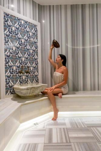 a woman sitting on a ledge drinking from a bottle at Blue Dreams Resort Bodrum - Aquapark & Ultra All Inclusive in Torba