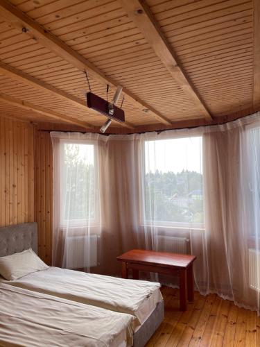a bedroom with a bed and a table and windows at Під лісом in Skhidnitsa