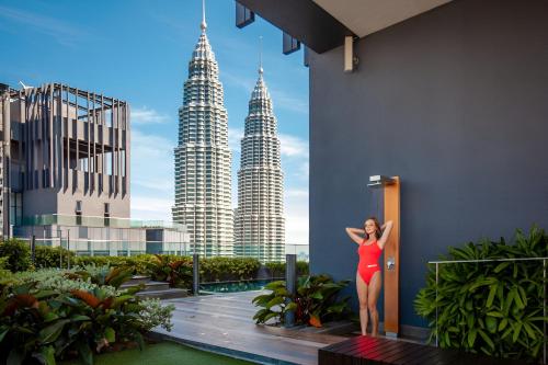 a woman in a red dress standing on a balcony with the petronas towers at Premier Suites Twin Towers at Star Residences in Kuala Lumpur