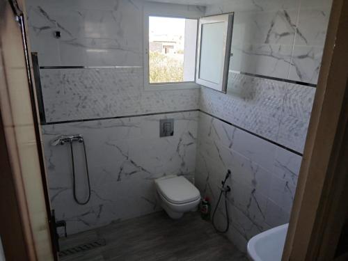 a white bathroom with a toilet and a window at Souhyla in Nabeul
