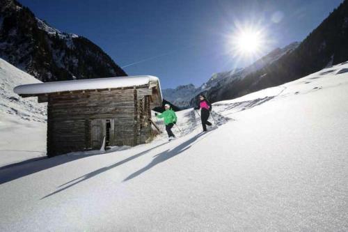 two people are standing in the snow next to a cabin at Apart Garber in Zellbergeben