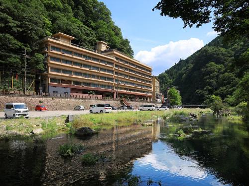 a large building with cars parked in front of a river at 湯原国際観光ホテル菊之湯 in Maniwa