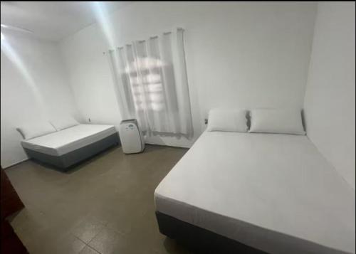 a white bedroom with two beds and a window at Casa Temporada in Rio das Ostras