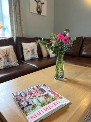 a vase of flowers on a table with a magazine at Swallow Cottage in Ripon