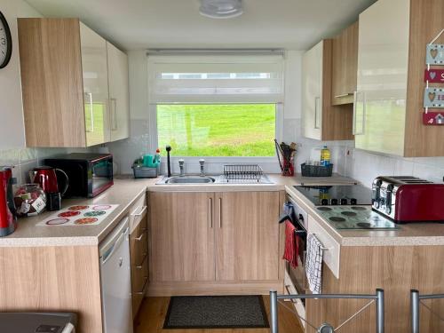 a kitchen with wooden cabinets and a sink and a window at 23 Sea Valley, Quiet Chalet at Bideford Bay holiday park in Bideford