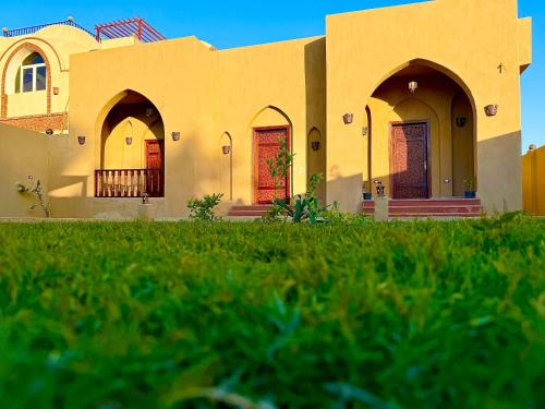 a yellow building with red doors and a grass field at Bab Al Shams Palace in Luxor